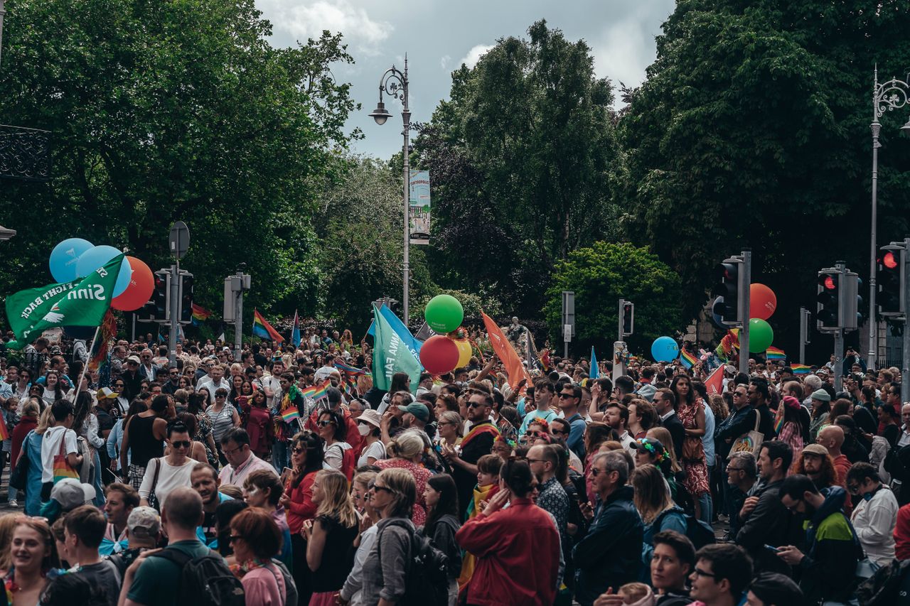 Large crowd gathered for an outdoor celebration with balloons and flags, enjoying a lively festival atmosphere.